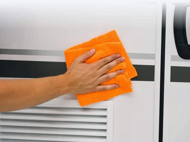 Oranje Carmotec microvezeldoek wrijft de wand van een camper na